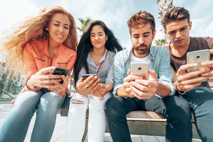 A group of 4 teenagers sat down scrolling through social media on their mobile phone
